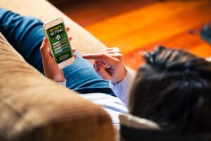 Woman holding a mobile phone to visit a sports betting website while lies down at home.