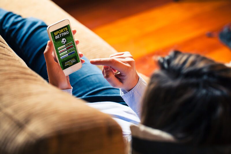 Woman holding a mobile phone to visit a sports betting website while lies down at home.