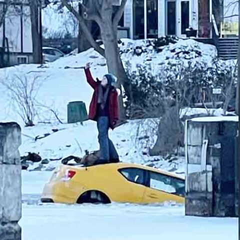 Woman stands on top of car to take selfie after driving it into frozen river - photo licensed by shore news network.