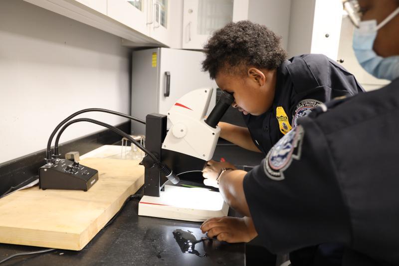 CBP Swears in 10-year-old Officer Daniel looks through a microscope