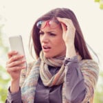 Annoyed upset woman in glasses looking at her smart phone with frustration while walking on a street. Photo by Chiosea