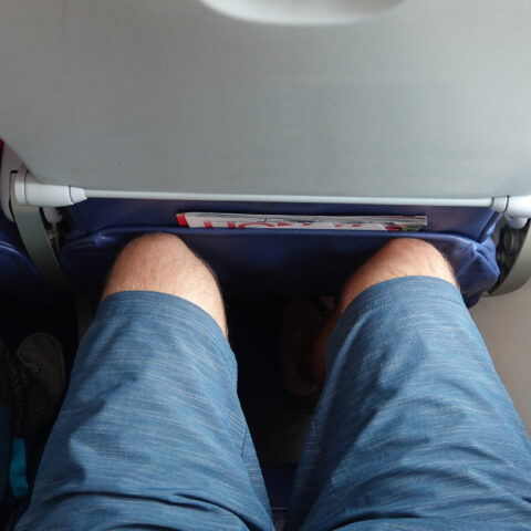 Pov: sitting in an uncomfortable economy class window seat with no leg room. Tourist on long transatlantic flight gets his legs jammed into the seat in front of him. Traveler enduring annoying flight.
