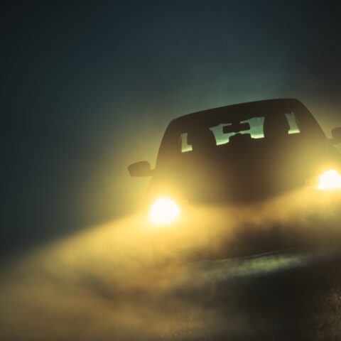 Car driving in dense fog. Dangerous road conditions. Night time driving in fog.