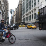 New York City, USA - July 25, 2018: Seventh Avenue and 34th Street with a cyclist with an electric bike and people around in Manhattan in New York City,