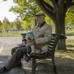 Old man and a little cute dog sitting and resting on bench on October 05,