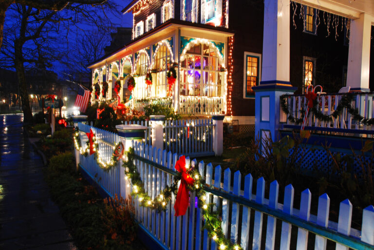 Christmas lights adorn a white picket fence bordering a stately Victorian home in Cape May, New Jersey - Photo by James Kirkikis