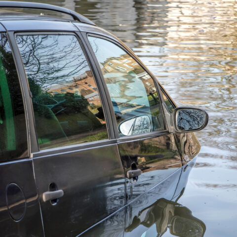 Car partially submerged in flood water on flooded road.