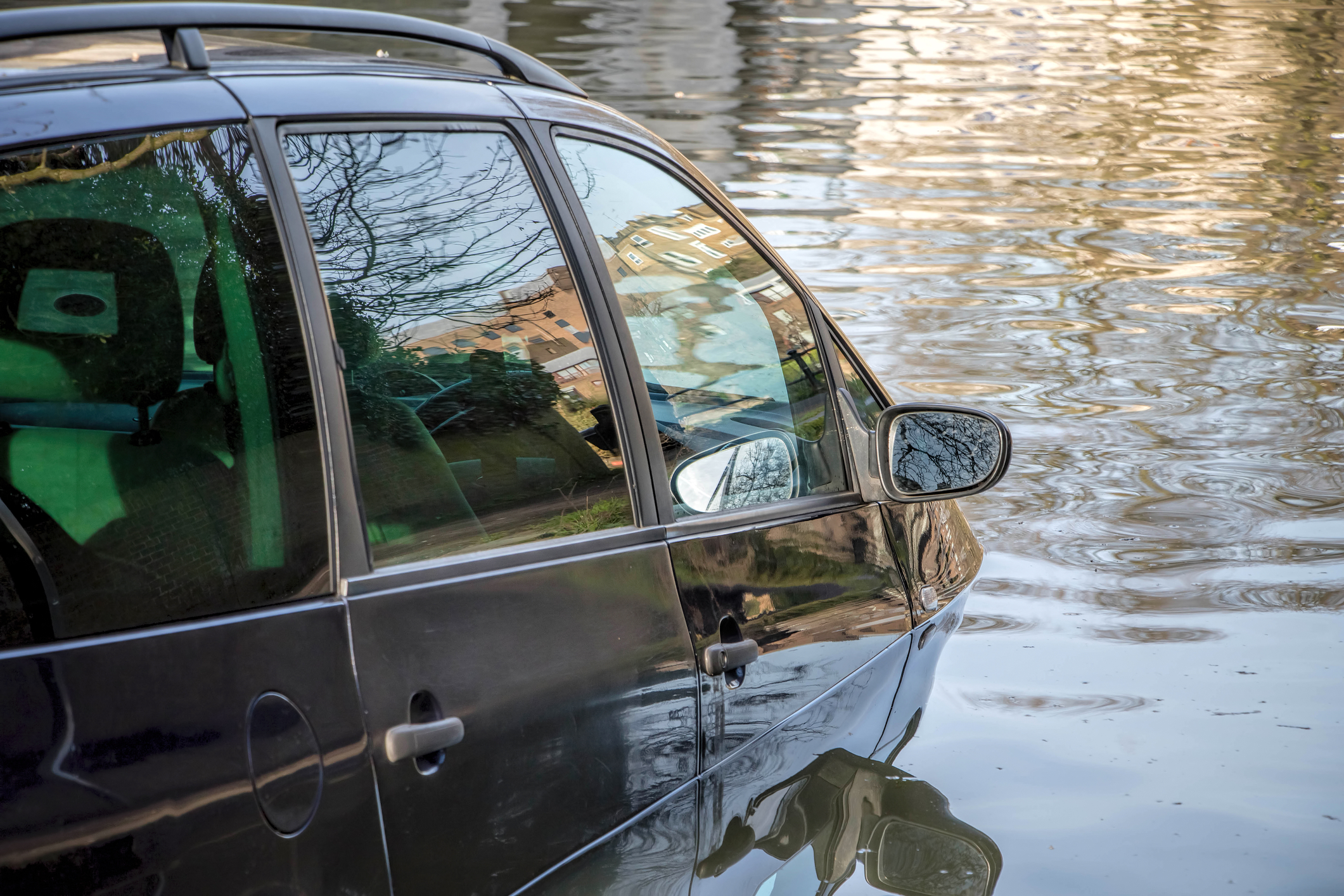 Car partially submerged in flood water on flooded road.