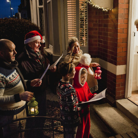 Three generation family are doing door-to-door carol singing. There is a senior women at the door, appreciating their singing.