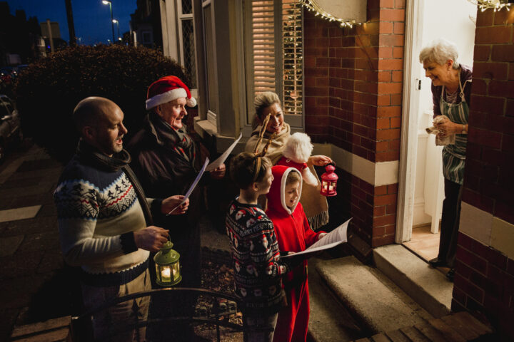 Three generation family are doing door-to-door carol singing. There is a senior women at the door, appreciating their singing.