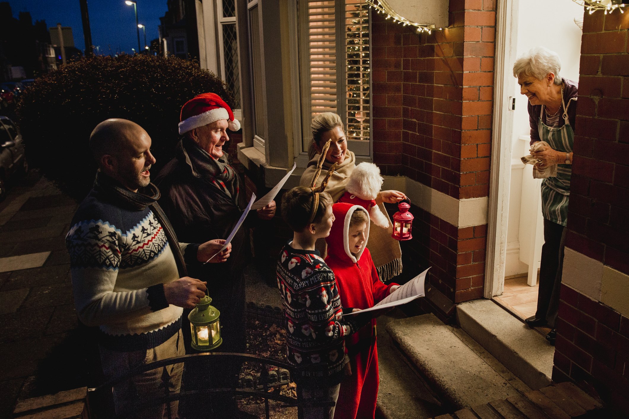 Three generation family are doing door-to-door carol singing. There is a senior women at the door, appreciating their singing.