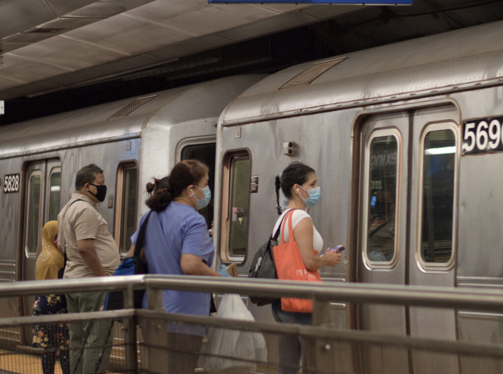 Commuters boarding a NYC subway train, wearing COVID-19 face masks