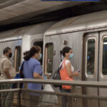 Commuters boarding a NYC subway train, wearing COVID-19 face masks