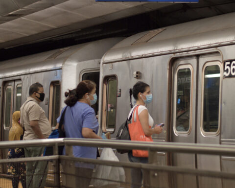 Commuters boarding a NYC subway train, wearing COVID-19 face masks