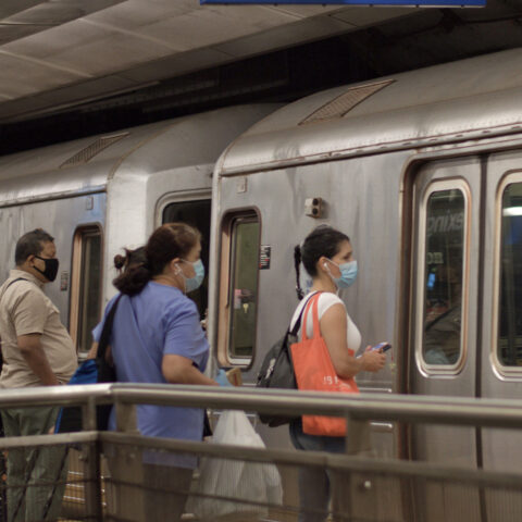 Commuters boarding a nyc subway train, wearing covid-19 face masks