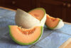 A cut up cantaloupe sitting on a slate tile kitchen counter top.