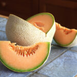 A cut up cantaloupe sitting on a slate tile kitchen counter top.
