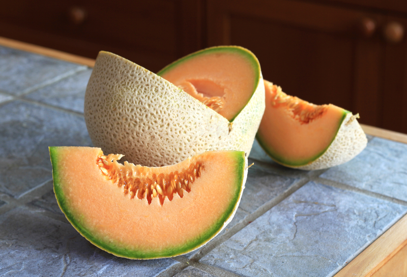 A cut up cantaloupe sitting on a slate tile kitchen counter top.