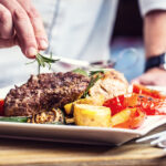 Chef in hotel or restaurant kitchen cooking only hands. Prepared beef steak with vegetable decoration