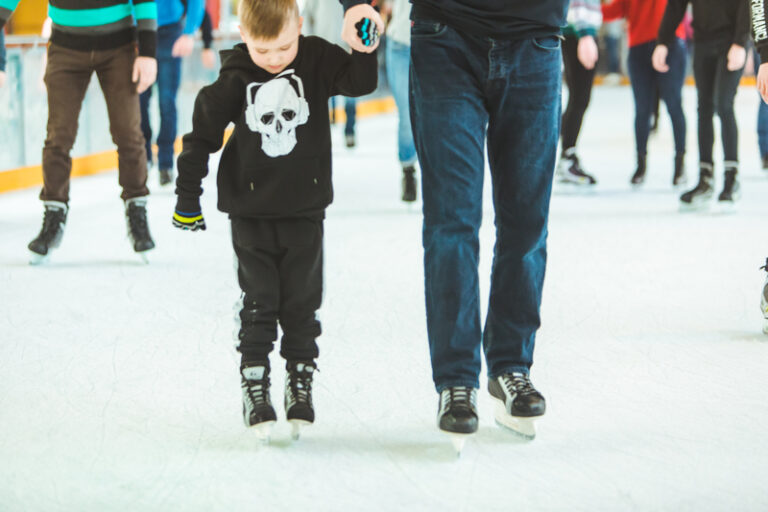 Child and father skating at ice rink.