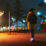 Woman walking alone near park in the city at night.
