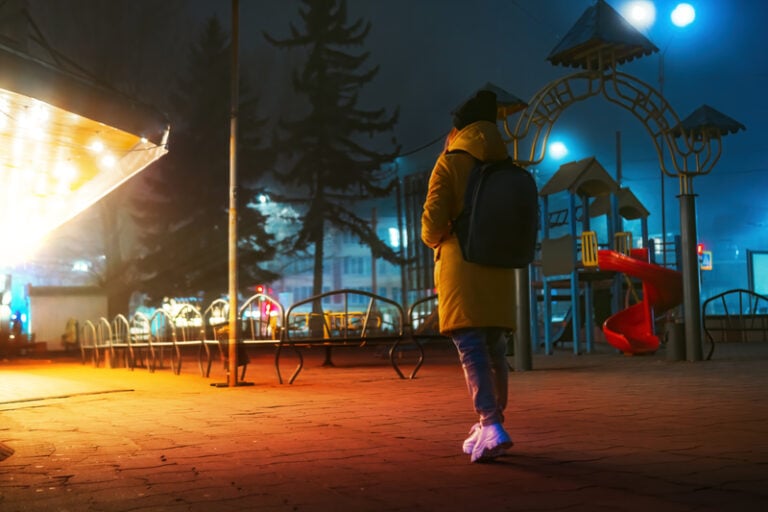 Woman walking alone near park in the city at night.
