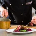 Chef in hotel or restaurant kitchen cooking, only hands, he is working on the sauce for the food as saucier, a Risotto