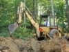 Operator using back hoe for excavating in forest.