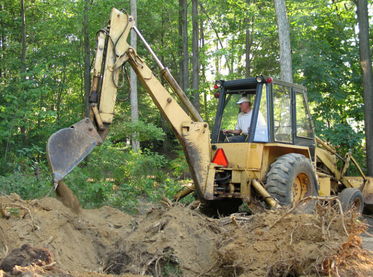 Operator using back hoe for excavating in forest.