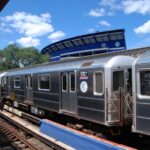 A #7 Flushing line subway train stopped at the Willets Point-Shea Stadium station with the old Shea Stadium in the background in the Borough of Queens, New York.