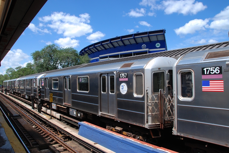 A #7 Flushing line subway train stopped at the Willets Point-Shea Stadium station with the old Shea Stadium in the background in the Borough of Queens, New York.