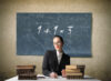 Portrait of a teacher sitting in front of a blackboard with a wrong addition written on it