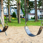 Playground with swings for children in the public park with houses in background.