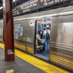 New York City subway station with passengers entering train, platform safety line and urban transit signage. New York. USA.