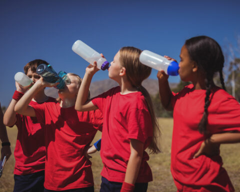Trainer and kids drinking water in the boot camp on a sunny day