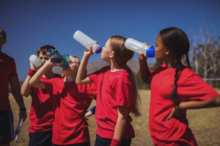 Trainer and kids drinking water in the boot camp on a sunny day