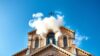 Vatican chimney releases white smoke to signal successful papal election. The Sistine Chapel chimney emits white smoke above the rooftops, framed by historic domes. Catholic tradition, timeless ritual, peaceful cityscape with religious significance.