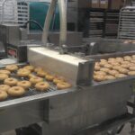 Donut making process. Dough of the doughnuts are being fried and transported on a conveyor belt