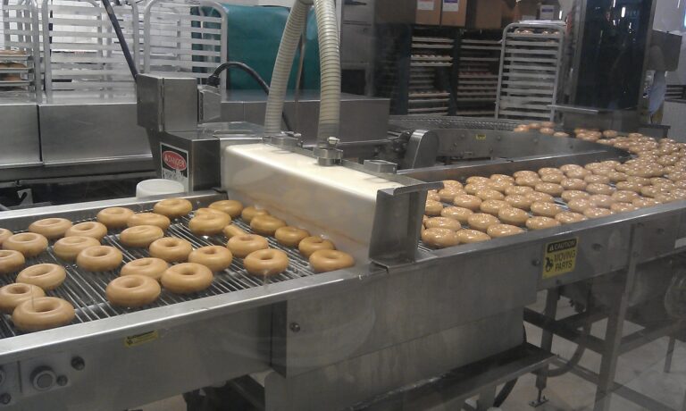 Donut making process. Dough of the doughnuts are being fried and transported on a conveyor belt