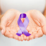 Hands holding purple awareness ribbon. Healthcare and social problems concept - womans hands holding purple domestic violence awareness ribbon.