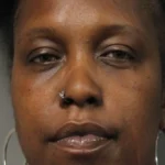 Close-up portrait of a Black woman with a nose ring and large hoop earrings, neutral expression.