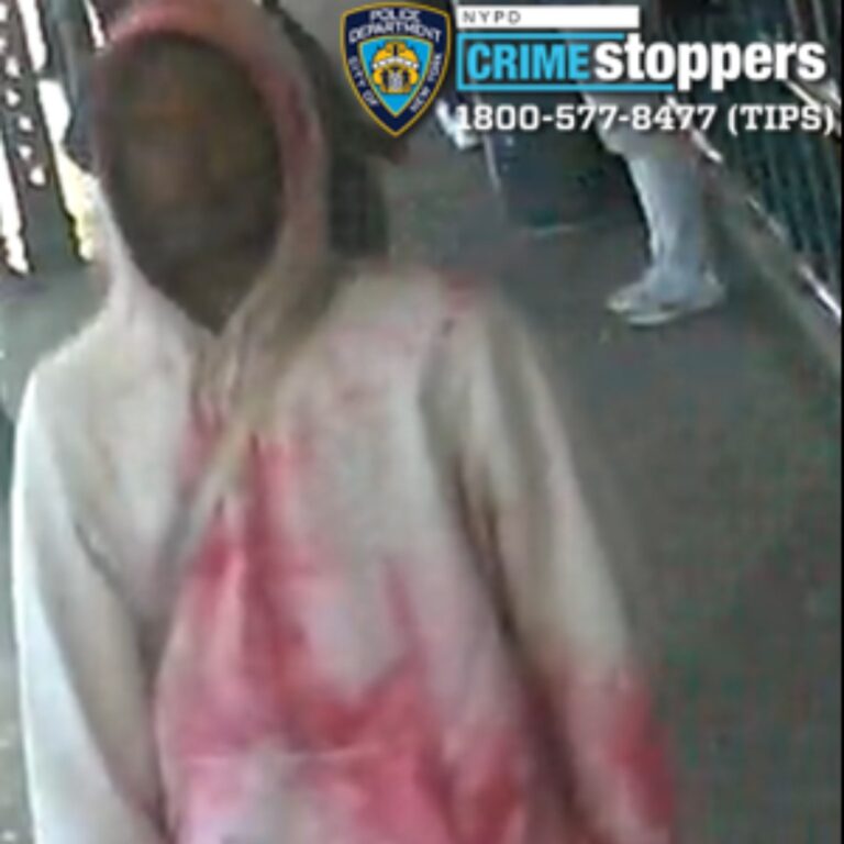 Surveillance image of a hooded person with face blurred, wearing a light-colored jacket and pink shirt, with a police badge overlay in the corner.