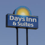 Days Inn & Suites sign featuring a blue panel with a yellow sunburst against a clear blue sky.