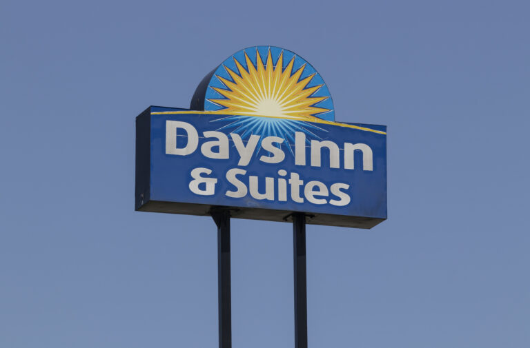 Days Inn & Suites sign featuring a blue panel with a yellow sunburst against a clear blue sky.