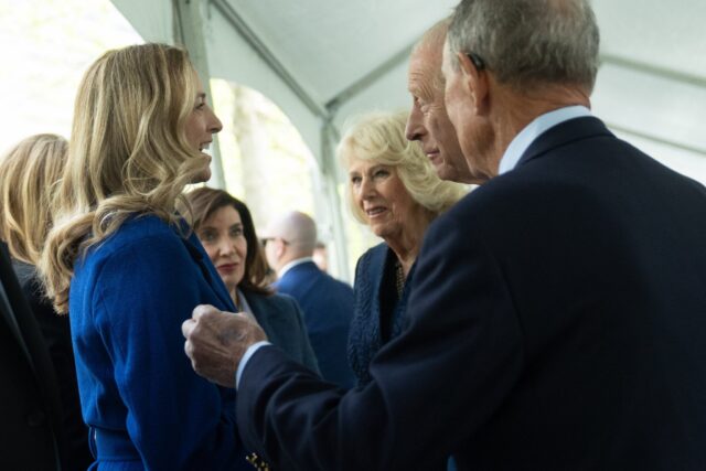 Businesspeople greeting with a handshake at a formal event; woman in blue jacket on the left, man in a dark suit on the right.