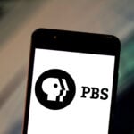 Close-up of a smartphone screen showing the PBS logo on a white background.