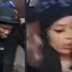 Surveillance-style image of two people: a man in a black coat and hat on the left, and a woman with dark hair and a head covering on the right in a dim setting.