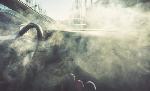 Smoke-filled car interior with a steering wheel and hazy dashboard partially visible.