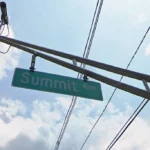 Street sign reading 'Summit Ave' hanging from a utility pole against a blue sky with traffic lights and power lines overhead.