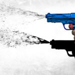 Hand holding a blue toy water gun spraying water to the left against a white background.